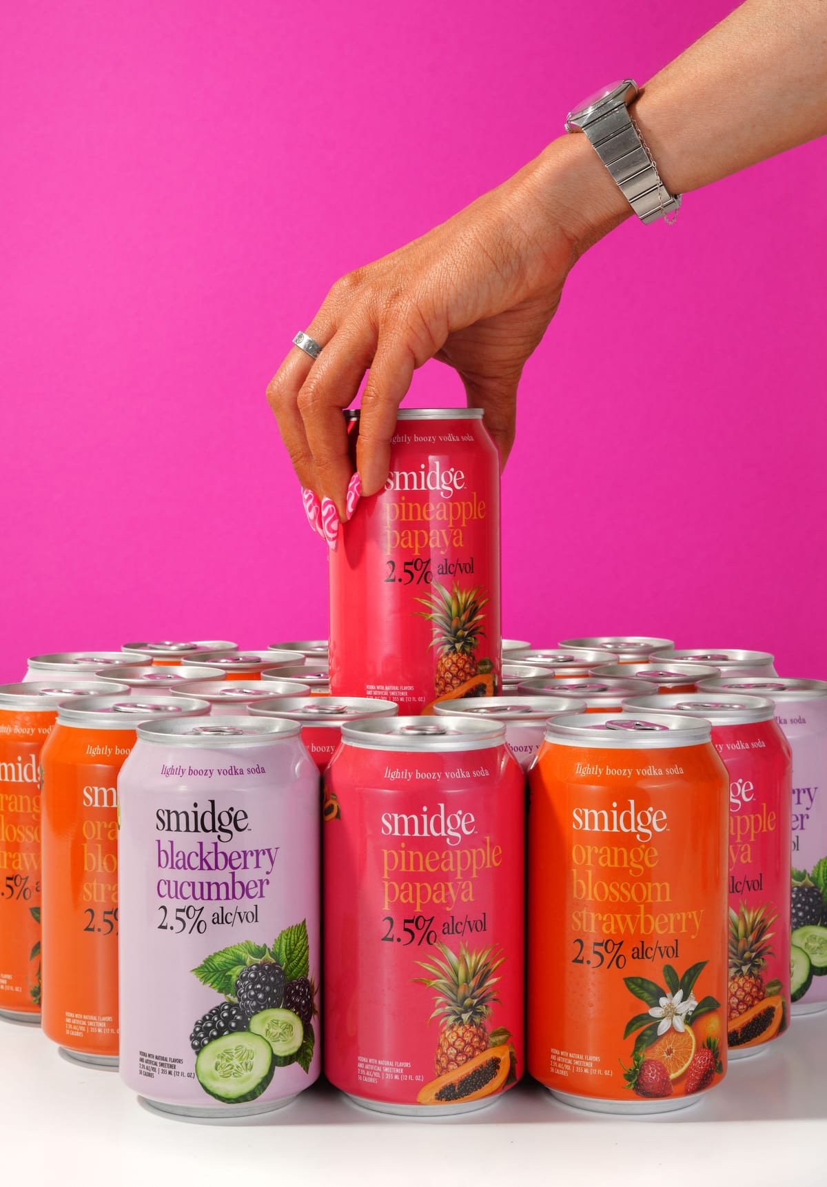 A hand grabbing a Smidge Pineapple Papaya can from a stack